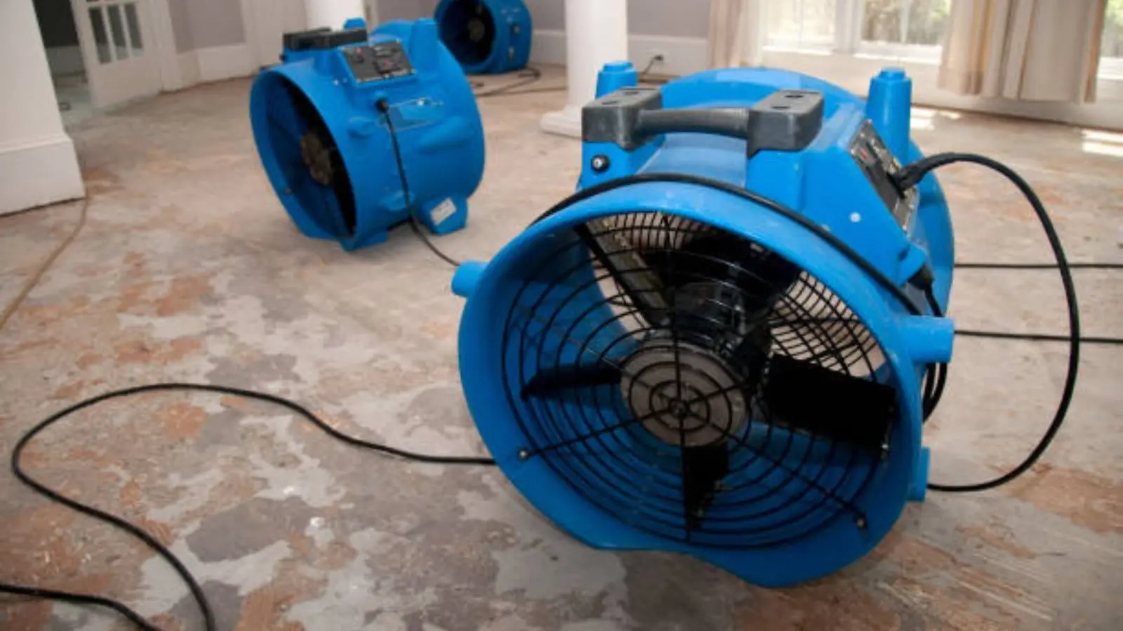 Blue air mover running on a damp floor with a power cord across the room
